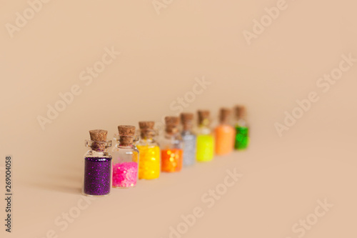 Colorful glitter in bottles on a beige background, isolated