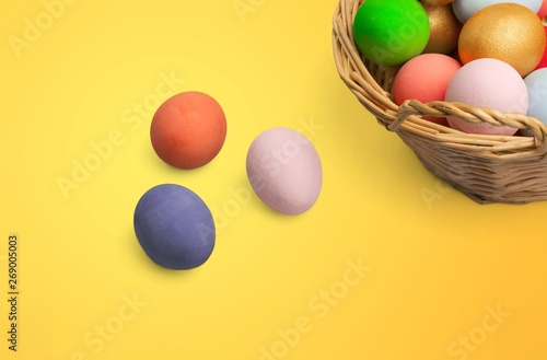Colorful Easter eggs in basket on yellow background
