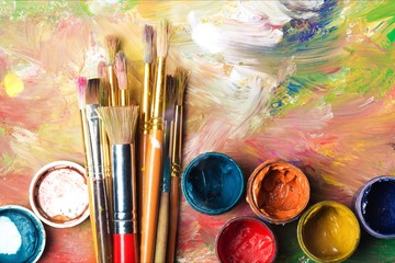 Artist paint brushes and paint cans of paint over bright watercolor background