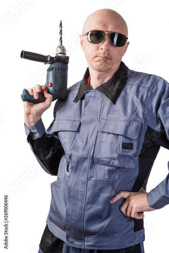 A man in working clothes, in dark protective glasses, with an electric drill in his hands