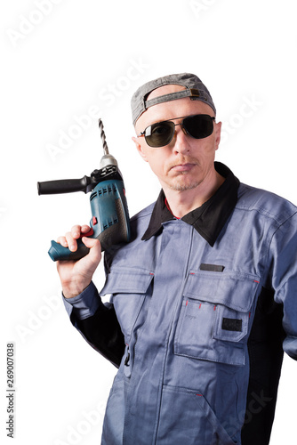 A man in working clothes, dark goggles and a cap, with an electric drill. A man of middle age, European appearance, in a working overalls. Isolated on white background