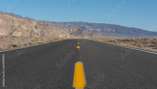 The straight and deserted road that leads to the Death Valley in California on a beautiful sunny winter day with a clear blue sky and background mountains