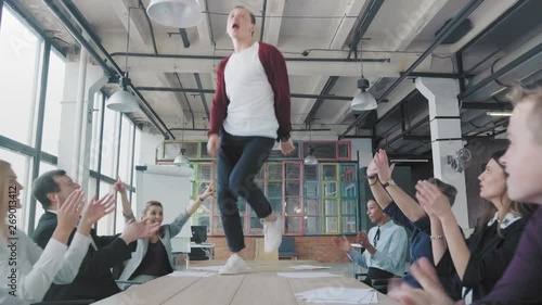 Employees celebrate the end of the project, have fun dancing on the table. His colleagues blow up flappers with confetti. Managers enjoy success and victory. Corporate party business team. Coworking