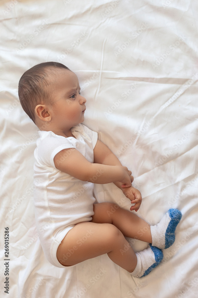 6-8-month-old baby boy lying playfully in bed. Charming 6-7 month little baby in white bodysuit. Baby boy in white bedding. Copy space 6-8-month-old baby boy lying playfully in bed. Charming 6-7 month little baby in white bodysuit. Baby boy in white bedding. Copy space