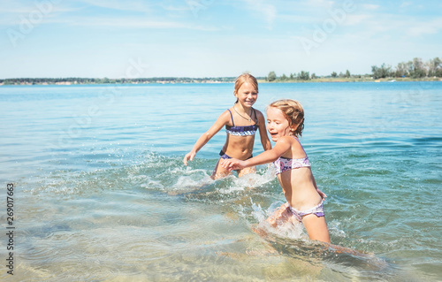 Two little sister girls fooling around in the calm sea waves splashing water to each other. Family vacation concept image.