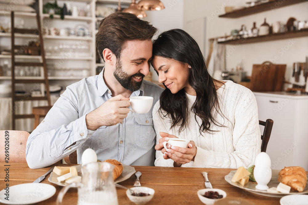 Portrait of lovely european couple eating at table while having breakfast in kitchen at home