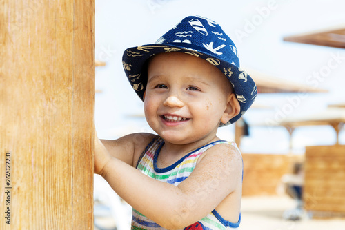 Portrait of a happy little cute boy of 1 or two years old wearing summer hat, playing on the beach of the hotel. Smiling laughing child with sand on his face and dirty hands. photo