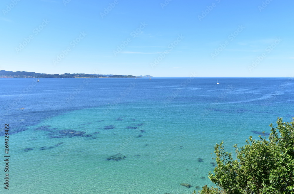 Bay with trees, turquoise water and sailing boats. Rias Baixas, Spain.