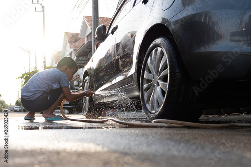 Asian children are using water hose to washing car in the mornign