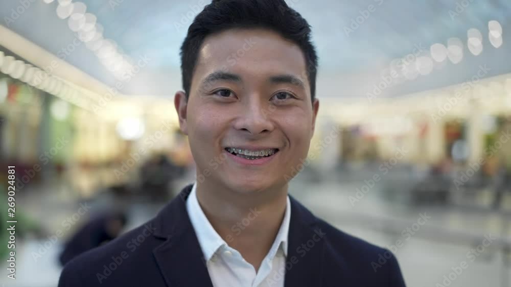 Gimbal shot close up portrait of asian male in business suit with braces smiling looking straight at camera on background of yellow bokeh effect Gimbal shot close up portrait of asian male in business suit with braces smiling looking straight at camera on background of yellow bokeh effect