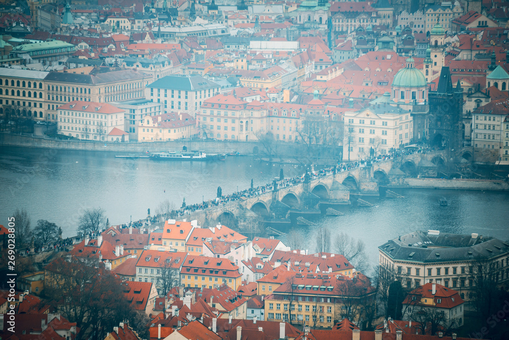 Fototapeta premium Beutiful view of the historical architectural buildings with red roofs and Charles bridge with tourists. View from an observation deck in Prague, Czhech Republic. Aerial top view