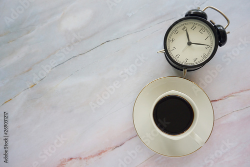 Cup of coffee and alarm clock on a marble textured background. photo