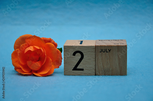 2 July on wooden blocks with an orange rose on a blue background