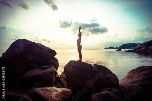 Sexy bikini women doing yoga stretch on rocky sea beach