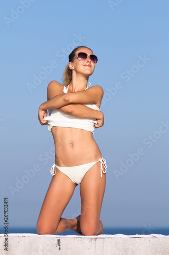 Young woman in sunglasses undressing and looking up