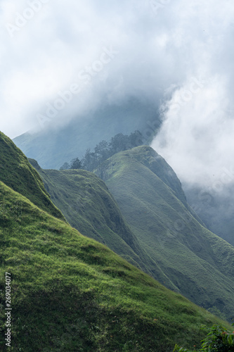 A lower part of Mount Rinjani showing lush green fields and a cloudy sky before rain on Lombok, Indonesia
