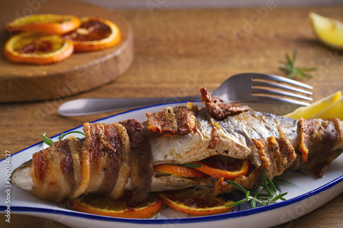Grilled bacon-wrapped fish with oranges and rosemary, served with lemons - Image