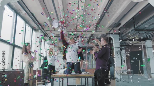 Manager start to dance on the table, sings into a megaphone, accelerates and slide on lap. Colleagues blow up flappers with confetti. Office celebration. Success. Corporate party business team