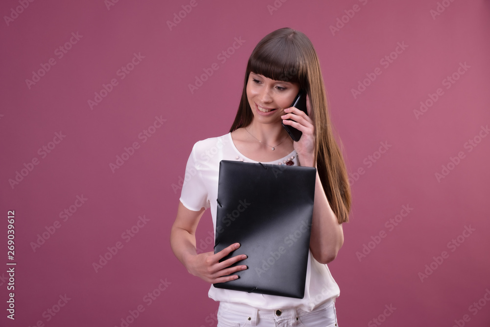 Image of young business woman standing over pink background looking aside chatting by phone holding folder. Image of young business woman standing over pink background looking aside chatting by phone holding folder.