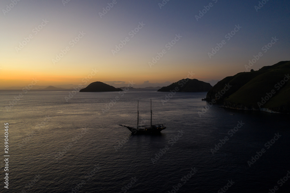A traditional Pinisi schooner sails at sunrise in Komodo National Park, Indonesia. This tropical area is known for its marine biodiversity as well as its dragons.