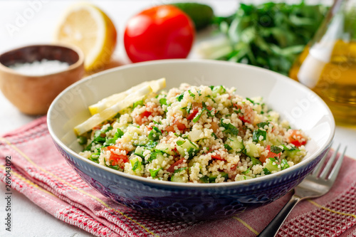 Traditional Arabic Salad Tabbouleh with couscous  vegetables and greens on concrete background. Selective focus.