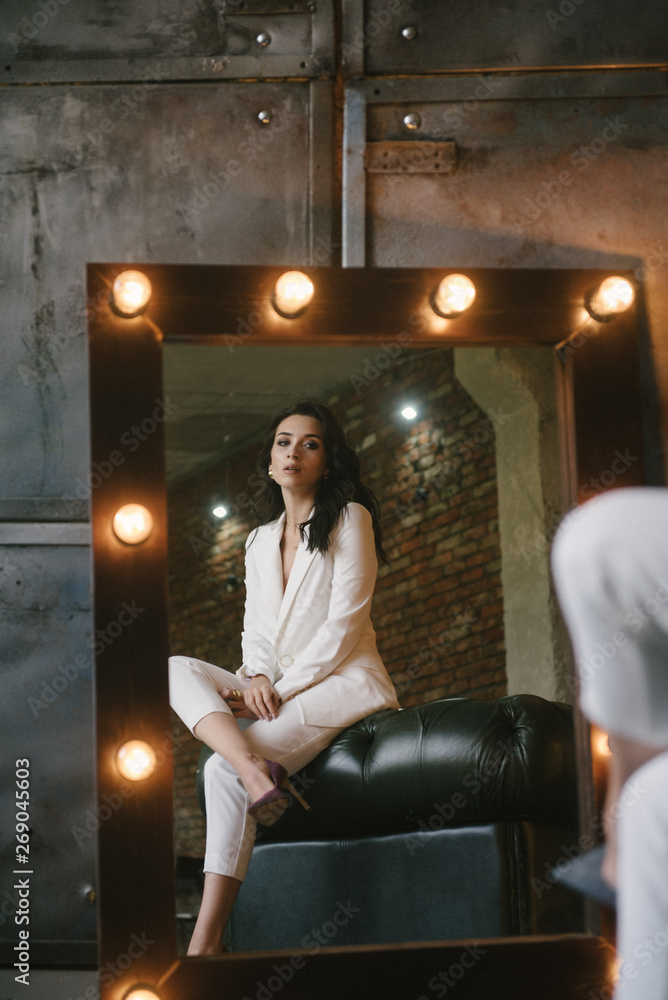 Young brunette woman posing in a suit sitting on a sofa