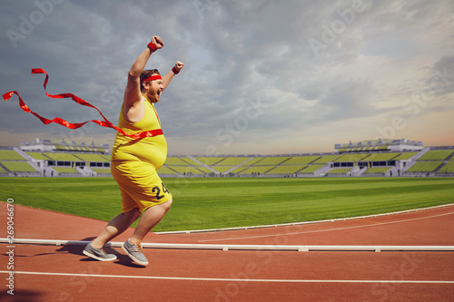 Fat funny man runs to the finish on track in the stadium.