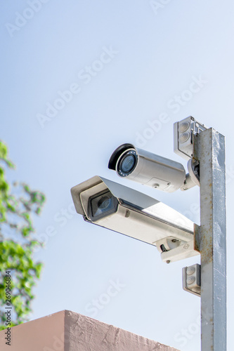 Two surveillance cameras on a pole against a blue sky.
