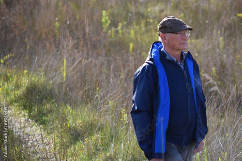 Canvastavla Hombre mayor con gorra paseando por el campo y observando el paisaje en un día soleado