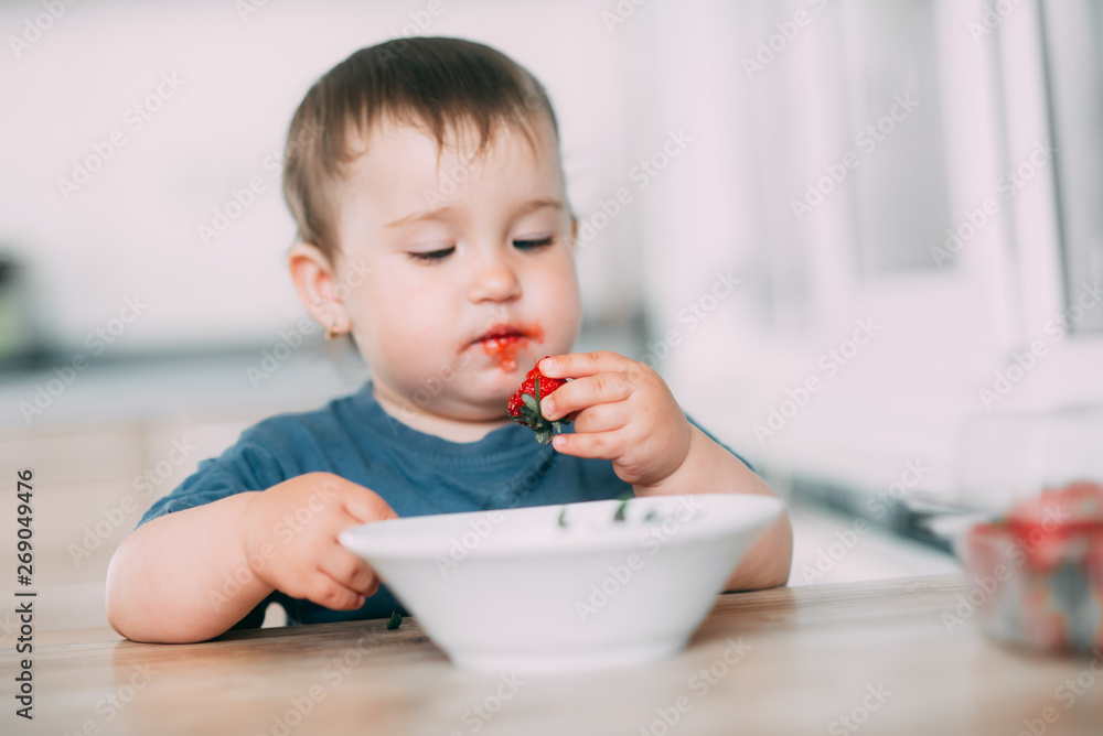 A little girl in the kitchen eating ripe strawberries very appetizing and tasty A little girl in the kitchen eating ripe strawberries very appetizing and tasty