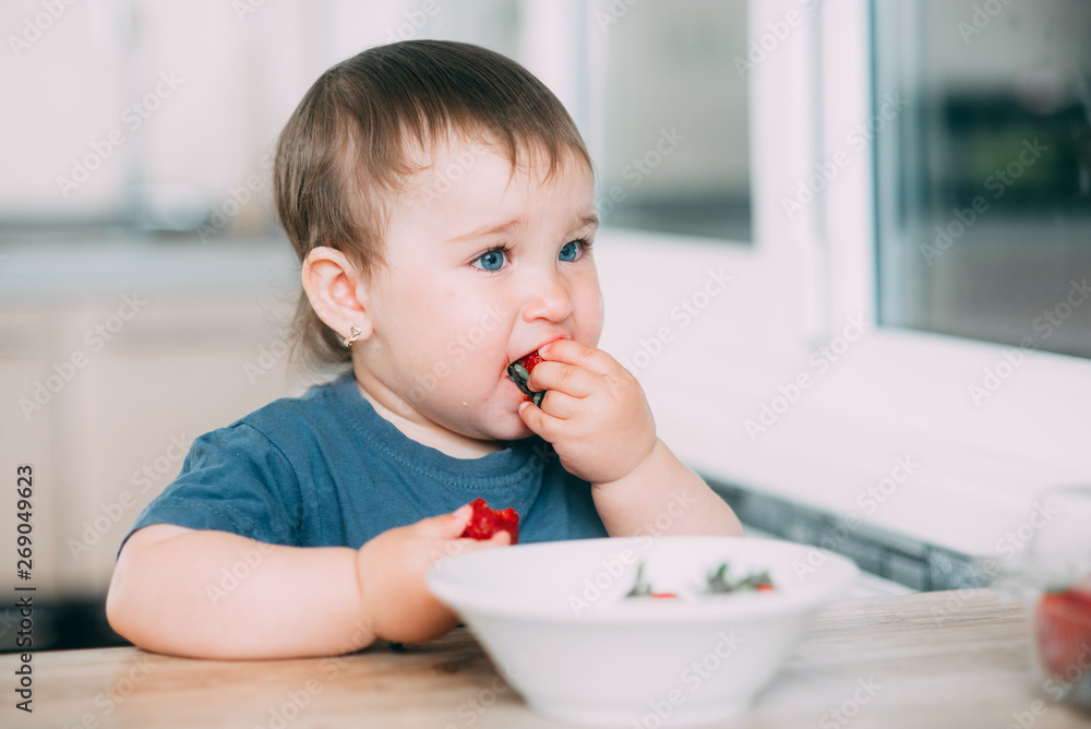 A little girl in the kitchen eating ripe strawberries very appetizing and tasty A little girl in the kitchen eating ripe strawberries very appetizing and tasty