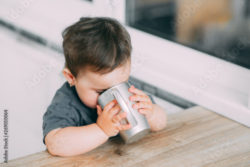 A little girl in the kitchen drinking water from a silver mug very greedily photo