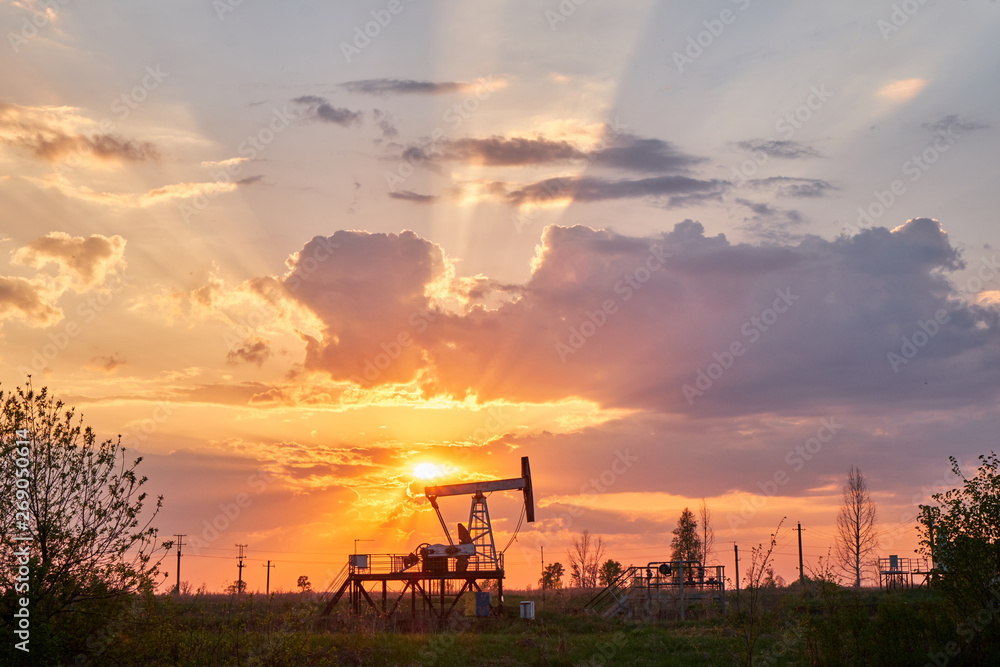 The equipment for oil and gas production works at sunset in the rays and glare of the sun. Oil well at sunset. Oil production with rocker at sunset. Rocking oil The equipment for oil and gas production works at sunset in the rays and glare of the sun. Oil well at sunset. Oil production with rocker at sunset. Rocking oil