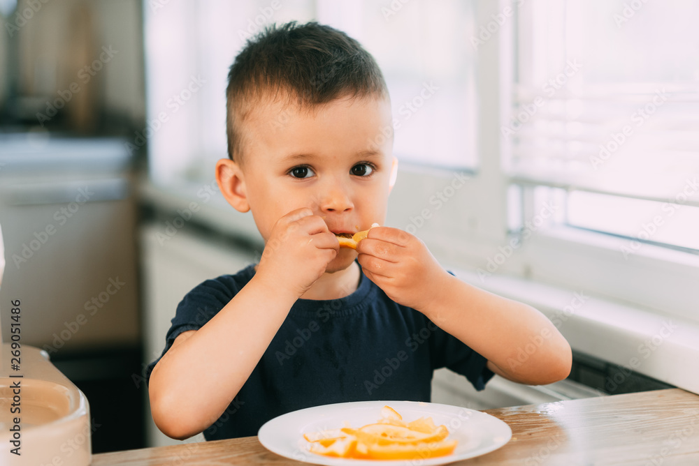 Beautiful Baby boy in the kitchen eagerly eating an orange, cut into wedges Beautiful Baby boy in the kitchen eagerly eating an orange, cut into wedges