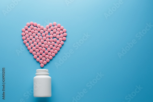Fototapeta Naklejka Na Ścianę i Meble -  Pink vitamins B12 pills in the shape of a heart on a blue background, poured out of a white can Low contrast