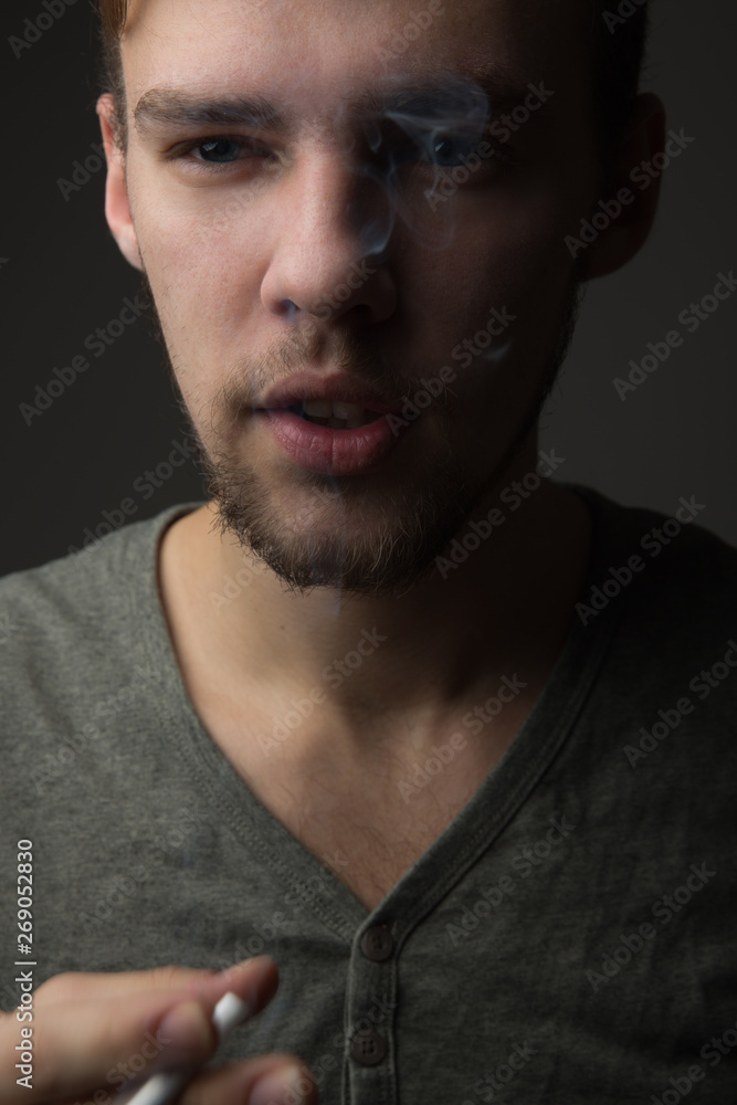 Portrait of a young Caucasian Smoking man with a short beard and mustache on a dark background