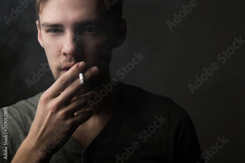 Portrait of a young Caucasian Smoking man with a short beard and mustache on a dark background