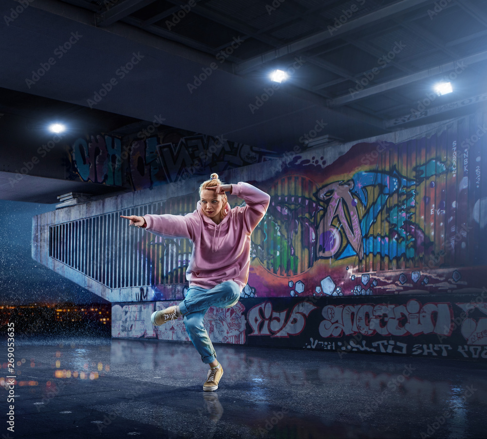 Female Hip Hop Dancer. Beautiful girl dancing at night on the background of graffiti wall