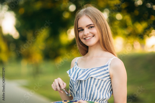 Portrait of Beautiful girl artist is standing in the park and holding palette with paints