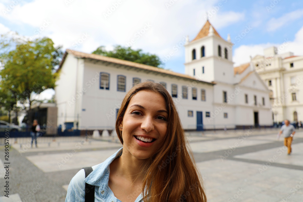 Happy smiling young woman in Sao Paulo city center with Patio do Colegio landmark on the background, Sao Paulo, Brazil