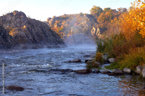 Wild mountain river with rapids flowing along rocky banks in wilderness. Morning autumn landscape of the river