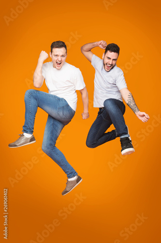 Two Friends Jumping And Celebrating Success Over Yellow Background