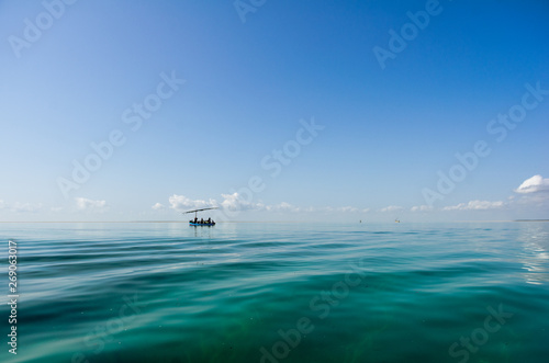 Tropical sea quiet blue sky with clouds and transparent water that allow to see the seaweed background. Fisherman's boat on the horizon.