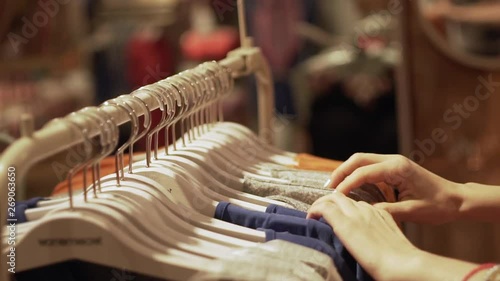 Close up of a girl goes through clothes dresses summer outfits and shop the boutique, the supermarket on the rack, close-up of hands and racks of clothes, shopping