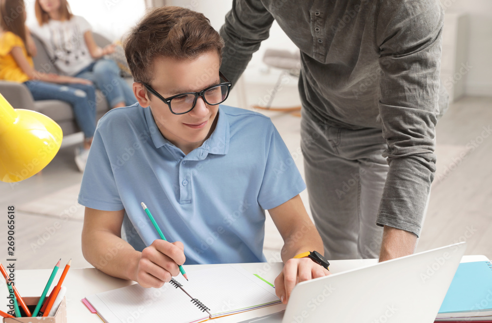 Father helping his teenager son with homework indoors Father helping his teenager son with homework indoors