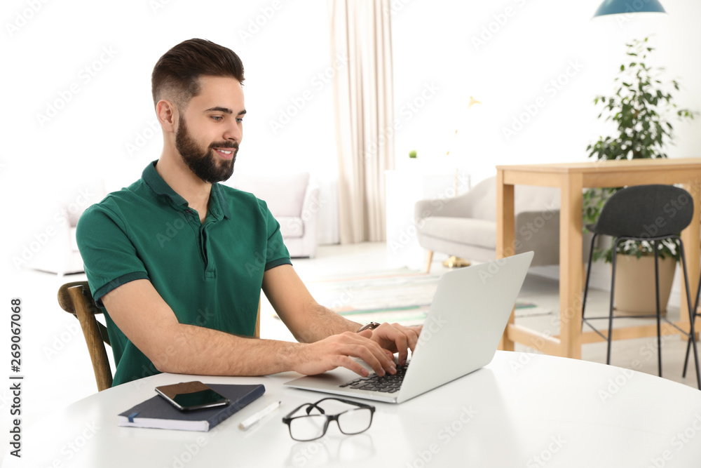 Handsome young man working with laptop at table in home office Handsome young man working with laptop at table in home office
