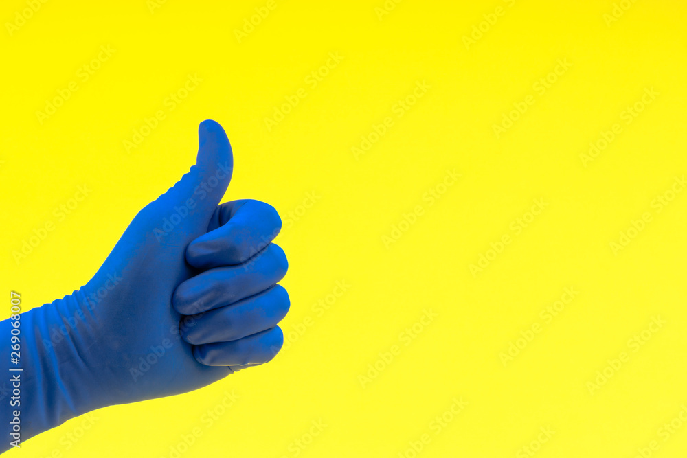 Hand in a blue glove with sign thumbs up or good on yellow background