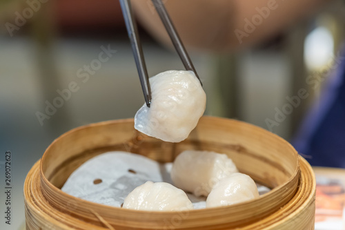 Fotografie Close up of chopstick holding dim sum Ha gow (traditional Cantonese dumpling) with wood basket