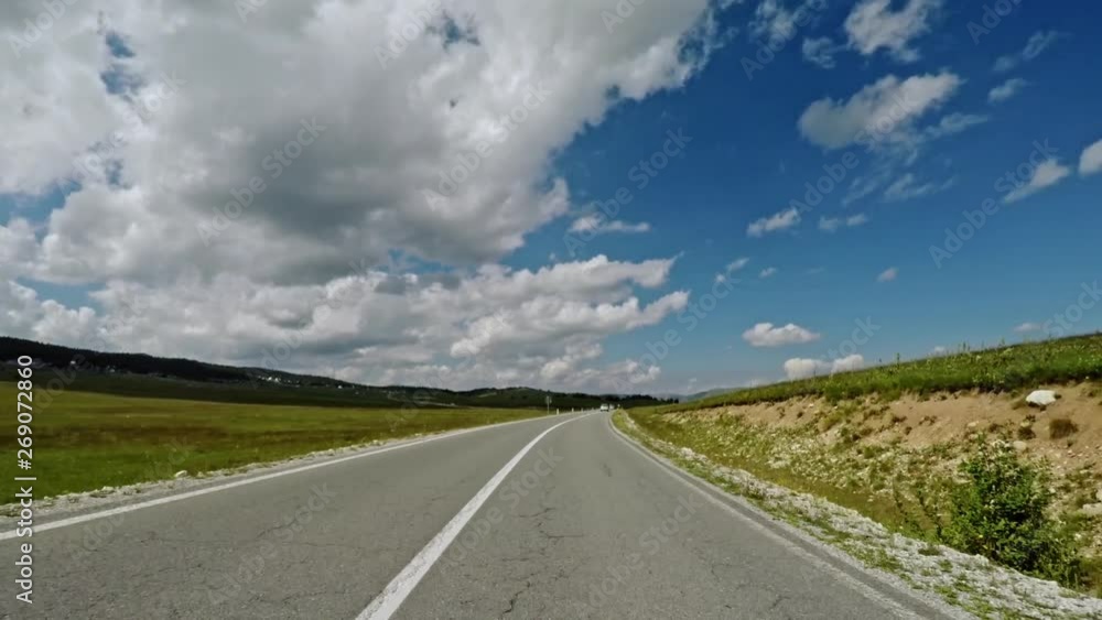 Camera moving over asphalt road trough green field against cloudy sky on sunny day in Montenegro nature. Camera moving over asphalt road trough green field against cloudy sky on sunny day in Montenegro nature.