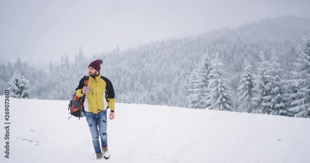Walking tourist through the snowy field, holding a cup with hot tea to get warm , beautiful landscape on background snowy forest and mountain
